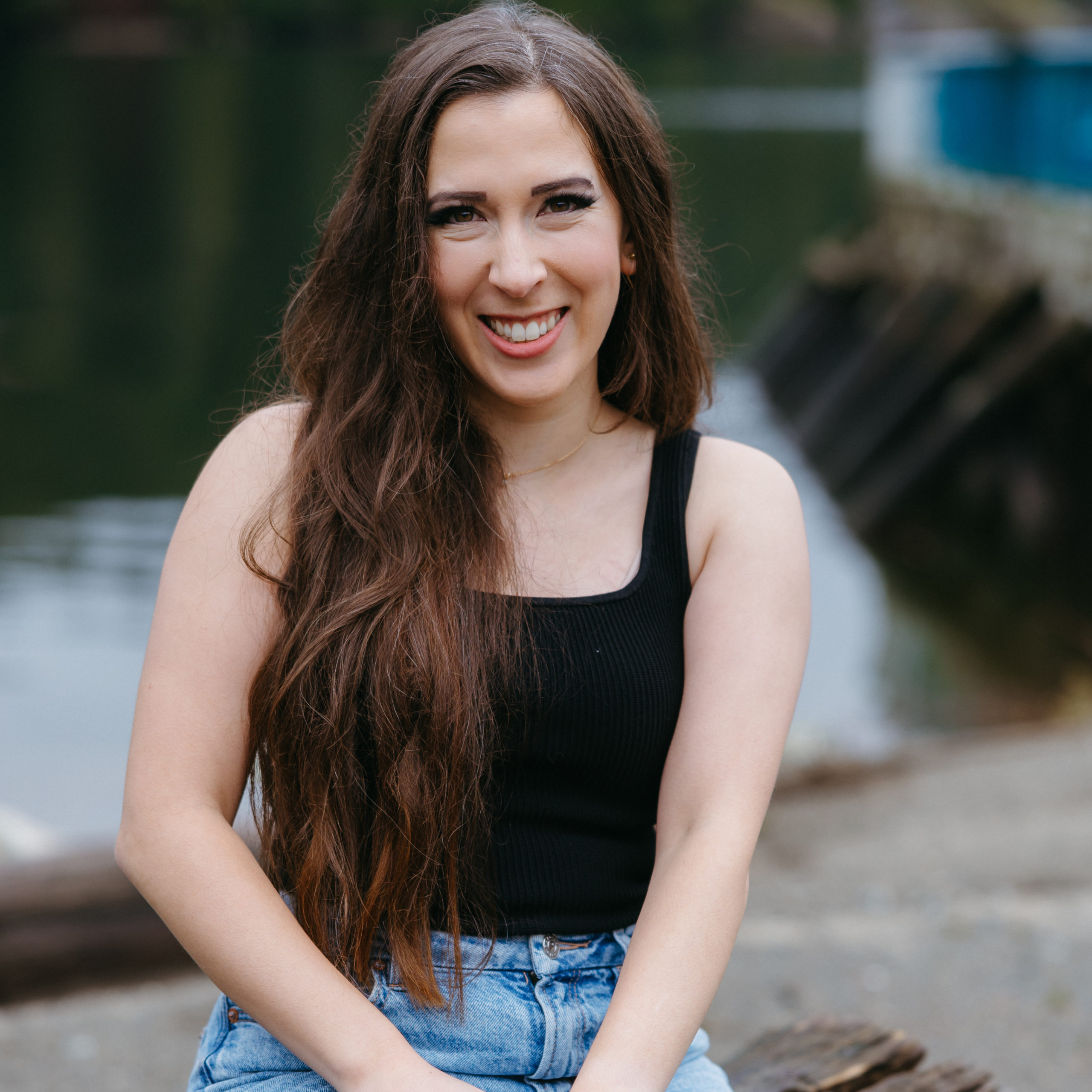 Photo of Ultrasaurus wearing a black tank top and blue jeans sitting on a log in front of a lake